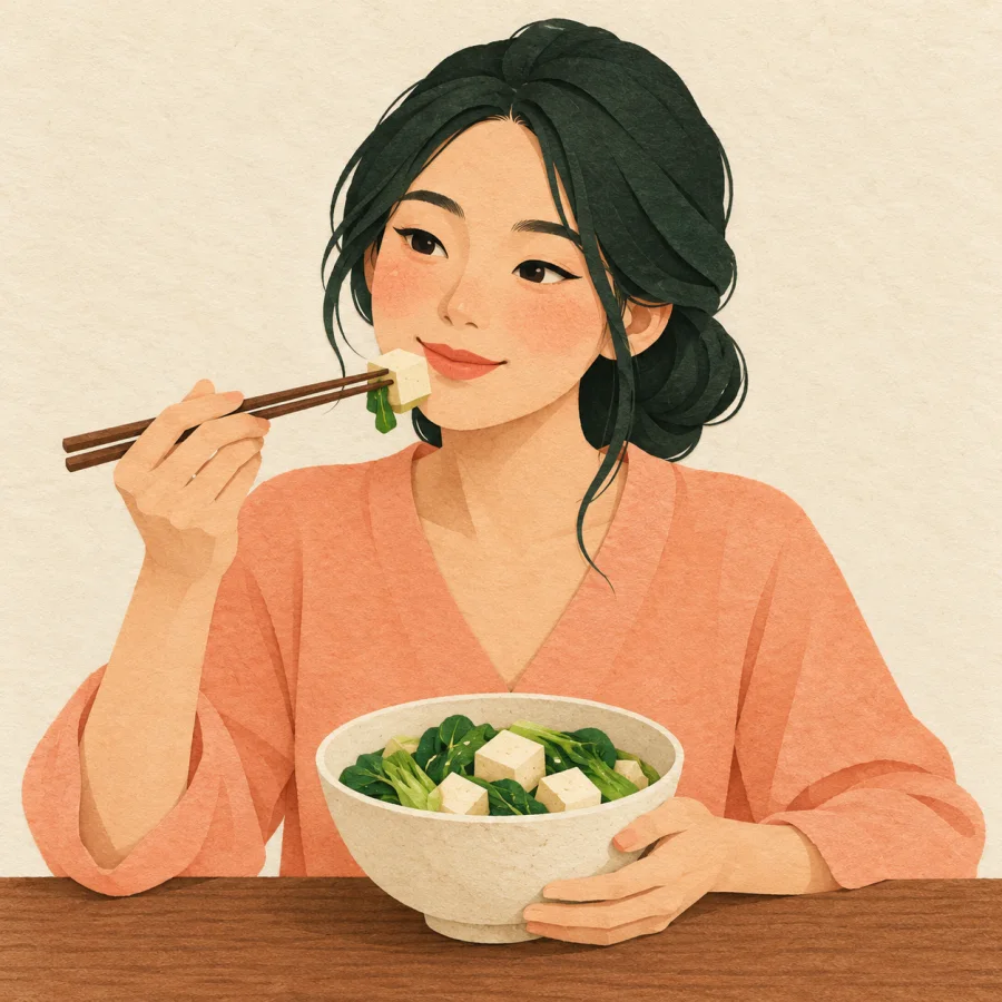 A woman eats vegetables and tofu at a plain wooden table